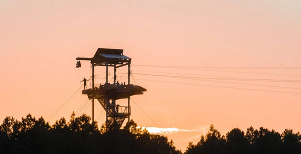 Zipline věž s lidmi siluety při západu slunce — Stock fotografie