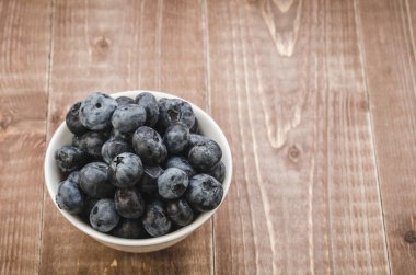 ahşap arka plan üzerinde beyaz bir kasede beyaz kase/taze yaban mersini taze yabanmersini. Üstten görünüm ve boşaltmak