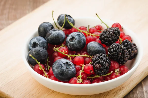 abundance of berries in a white bowl/ abundance of berries in a white bowl on a wooden surface. Selective focu