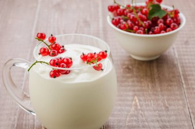 yoğurt ve bir ahşap arka plan/yoğurt ve ahşap arka plan üzerinde beyaz bir kase kırmızı kuş üzümü üzerinde beyaz bir kase kırmızı kuş üzümü. seçici odak