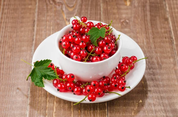 white cup full of red berries/white cup full of red berries on a wooden background. Selective focus
