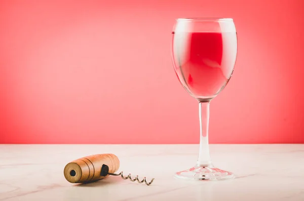 Wine glass and corkscrew on pink background/Wine glass and wooden corkscrew on pink  background. Selective focu