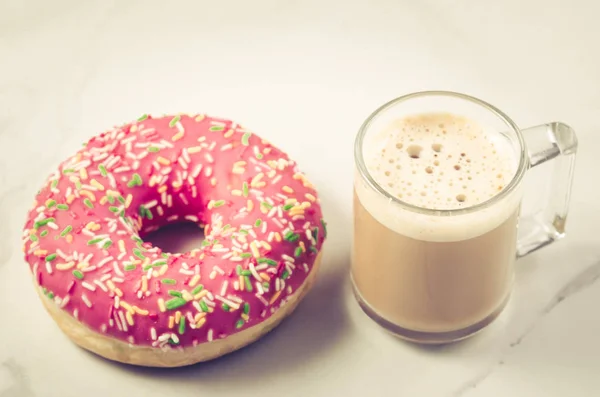 咖啡休息 卡布奇诺玻璃与新鲜的含糖粉红色甜甜圈 咖啡休息 卡布奇诺玻璃与新鲜的甜粉色甜甜圈在白色大理石背景 — 图库照片