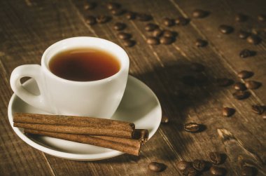 beyaz fincan kahve, tarçın çubukları ve kahve çekirdekleri/beyaz fincan kahve, koyu ahşap zemin üzerine tarçın ve kahve fasulye sopa. Kopya alanı