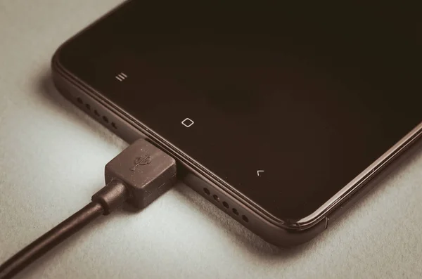 black smartphone with connected charger/black smartphone with connected charger. Toned