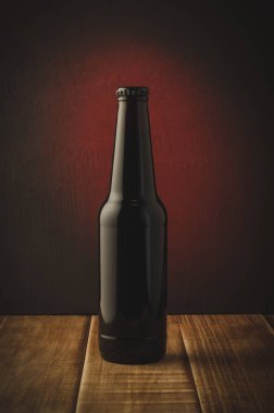 siyah şişe bira bira bir ahşap raf kırmızı bir arka plan üzerinde kırmızı arka plan/siyah şişe üzerinde. Seçici odak