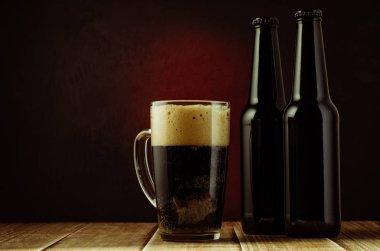 Ahşap raf/siyah şişe ve bardak bira bir ahşap raf kırmızı bir arka plan üzerinde kırmızı bir arka plan üzerinde siyah şişe ve bardak bira. Boşaltmak