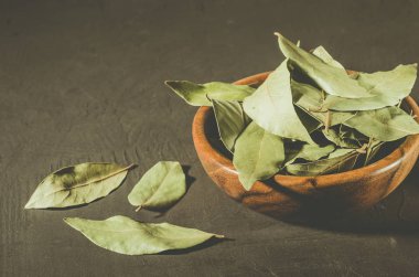 defne yaprağı üzerinde siyah bir taş zemin üzerine ahşap bir kabın içinde karanlık bir yüzey/defne yaprağı. seçici odak