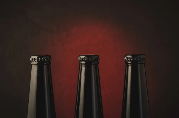 three black bottles of beer on a dark background with red light/three black bottles of beer on a dark background with red light. Selective focus