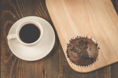 siyah kahve fincanı, çikolatalı muffin/sade kahve Kupası, çikolatalı kek ve ahşap tepsi. Üstten görünüm