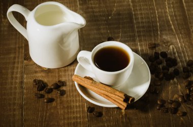 kahve fincanı, krema tarçın ile dağınık kahve çekirdekleri/fincan kahve, krema tarçın bir ahşap arka plan üzerinde dağınık kahve fasulye ile. Üstten görünüm