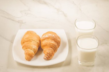 kruvasan ve süt/kruvasan bir beyaz plaka ve iki bardak süt beyaz zemin üzerine Odaya Servis Kahvaltı. Seçici odak