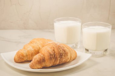 kruvasan ve süt/kruvasan bir beyaz plaka ve iki bardak süt mermer zemin ile kahvaltı. Seçici odak