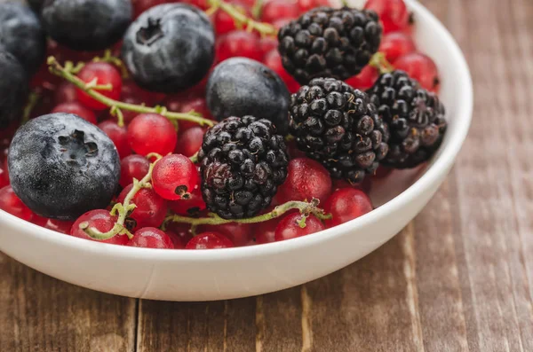 abundance of berries in a white bowl/ abundance of berries in a white bowl on a wooden background. Close up