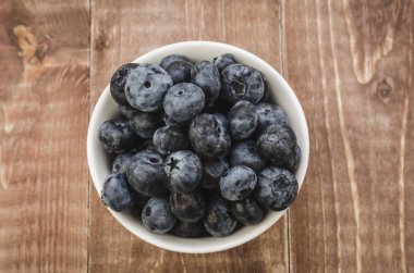 ahşap arka plan üzerinde beyaz bir kasede beyaz kase/taze yaban mersini taze yabanmersini. Üstten görünüm