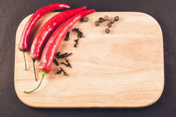 Red hot chili peppers and spices on a empty cutting board/Red hot chili peppers and spices on a empty cutting board on a dark background. Top view