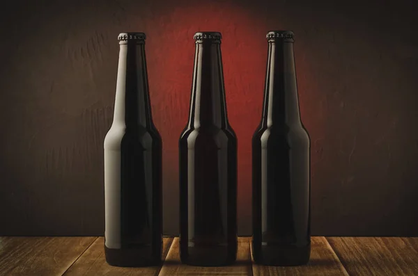 Three black bottle of beer on a red background of a wooden shelf/Three black bottle of beer on a red background of a wooden shelf. Selective focus