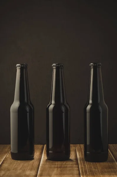 Three bottles of beer on a dark background of a wooden shelf/Three bottles of beer on a dark background of a wooden shelf, selective focus