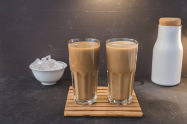 Tahta bir zeminde iki bardak sütlü kahve. Koyu arkaplanda tahta tepside iki bardak kahve.