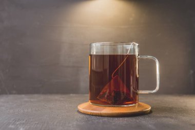 Cam bardaktaki çay poşeti ahşap bir stantta ve siyah bir masada cam bardaktaki siyah çay poşeti. Boşluğu kopyala.