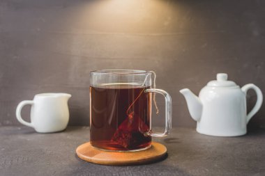 Tahta destekli bir fincan çay, siyah masadaki çaydanlık ve krema, tahta destekli bir fincan çay, siyah masadaki beyaz çaydanlık ve krema.