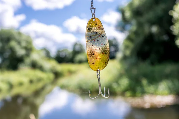 shine for fishing hangs/metal bait for fishing on the background of the river.