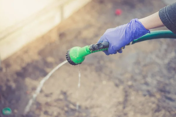 Hand in glove holds watering hose/hand in a rubber protective glove holds a watering, green hose with a green spray nozzle.