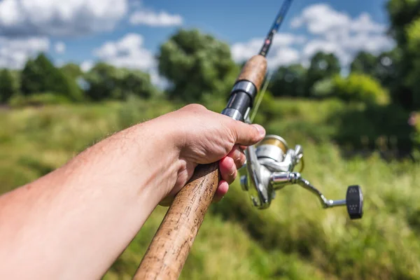 回転釣りの背景に男性の手を回転ロッドを保持します 男の手は日当たりの良いDaに川の背景に回転棒を保持しています — ストック写真