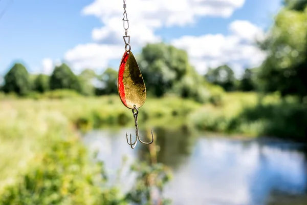 shine for fishing hangs/metal bait for fishing on the background of the river.