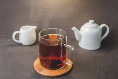 Tahta destekli bir fincan çay, siyah masadaki çaydanlık ve krema, tahta destekli bir fincan çay, siyah masadaki beyaz çaydanlık ve krema.