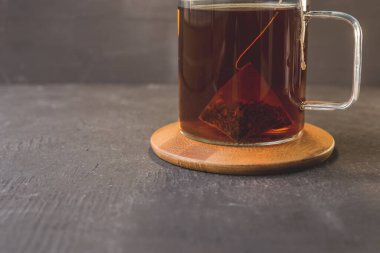 Cam bardaktaki çay poşeti ahşap bir stantta ve siyah bir masa / bir poşet çay bir cam fincanda ve siyah bir masada.
