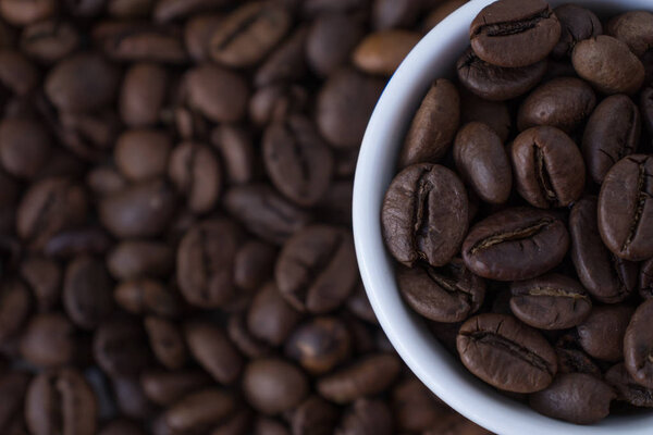 White cup full of coffee beans on the background of coffee beans. Close up