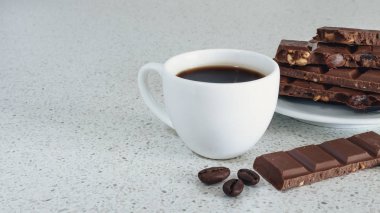 Bir beyaz taş tabloda siyah kahve ve çikolata, kahve çekirdekleri ile beyaz fincan