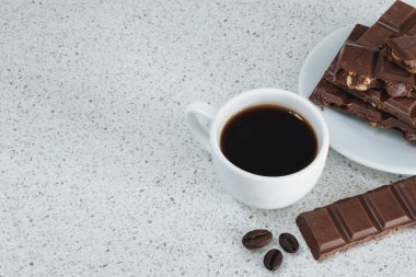 Bir beyaz taş tabloda siyah kahve ve çikolata, kahve çekirdekleri ile beyaz fincan