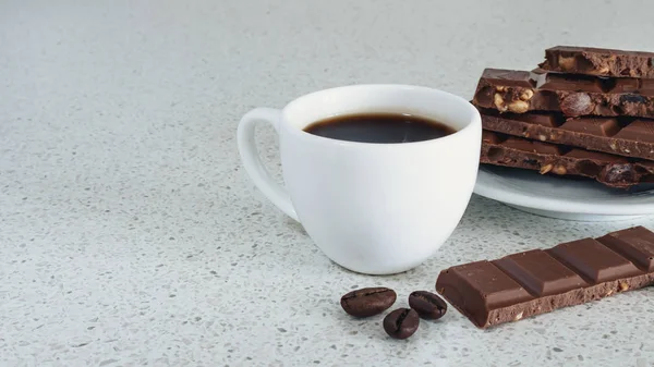 Bir beyaz taş tabloda siyah kahve ve çikolata, kahve çekirdekleri ile beyaz fincan