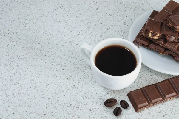 Bir beyaz taş tabloda siyah kahve ve çikolata, kahve çekirdekleri ile beyaz fincan