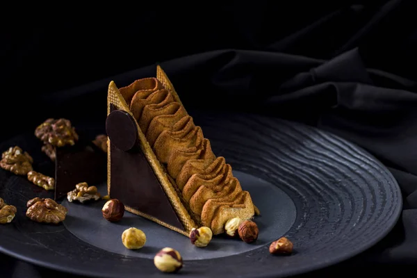 Piece of chocolate cakewuth nuts. Chocolate mousse cake on a black plate, black background.