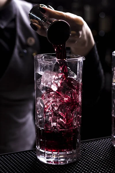 Bartender making refreshing coctail on a bar background. Dark moody style. Ice in tha glass