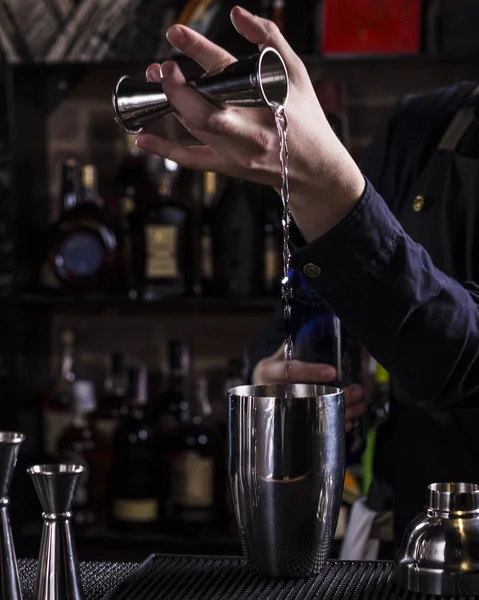 Bartender making refreshing coctail on a bar background. Dark moody style. Ice in tha glass