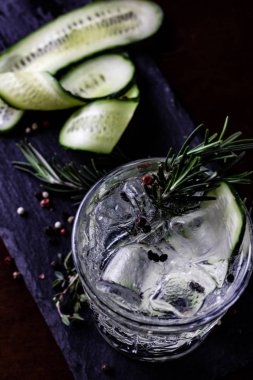 Cin-tonik alkollü kokteyl. Salatalık, biberiye, buz. Siyah bir ahşap arka plan üzerinde.