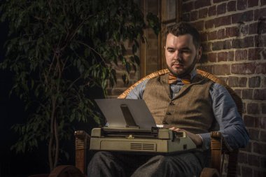 Sallanan sandalye brickwall arka plan üzerinde bir daktilo kullanan genç Hipster adam