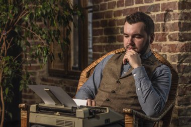 Sallanan sandalye brickwall arka plan üzerinde bir daktilo kullanan genç Hipster adam