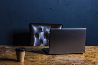 Masanın üstüne boş dizüstü kadar alay. Ahşap masa siyah duvar arka plan üzerinde kişisel dizüstü bilgisayar.