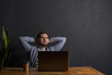 İş ile memnun. Mutlu genç adam Office çalışma evinde otururken dizüstü bilgisayarda çalışıyor. Koyu arka plan. Metin için yer