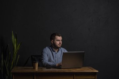 Genç işadamı ahşap masa üstünde onun laptop üzerinde çalışıyor. Metin için yer. Koyu arka plan. Metin için yer