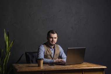 Genç işadamı ahşap masa üstünde onun laptop üzerinde çalışıyor. Metin için yer. Koyu arka plan. Metin için yer