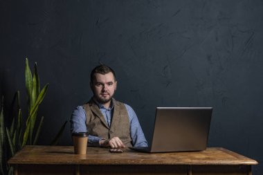 Genç işadamı ahşap masa üstünde onun laptop üzerinde çalışıyor. Metin için yer. Koyu arka plan. Metin için yer