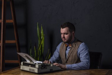 Daktiloda yazmaya sakallı şık yazar. Modern yazar ofiste yeni bir kitap üzerinde çalışıyor. Koyu arka plan. Metin için yer