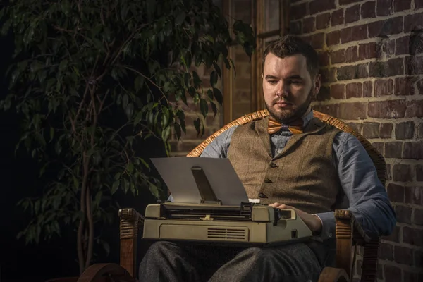 Young Hipster man using a typewriter at rocking chair on brickwall background