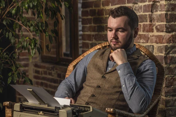 Young Hipster man using a typewriter at rocking chair on brickwall background